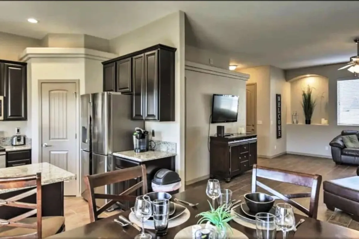 An open-plan area that seamlessly combines the kitchen island, a dining table set for a meal, and a view into the living room area. The space is styled for family gatherings, entertaining, and quiet moments alike.
