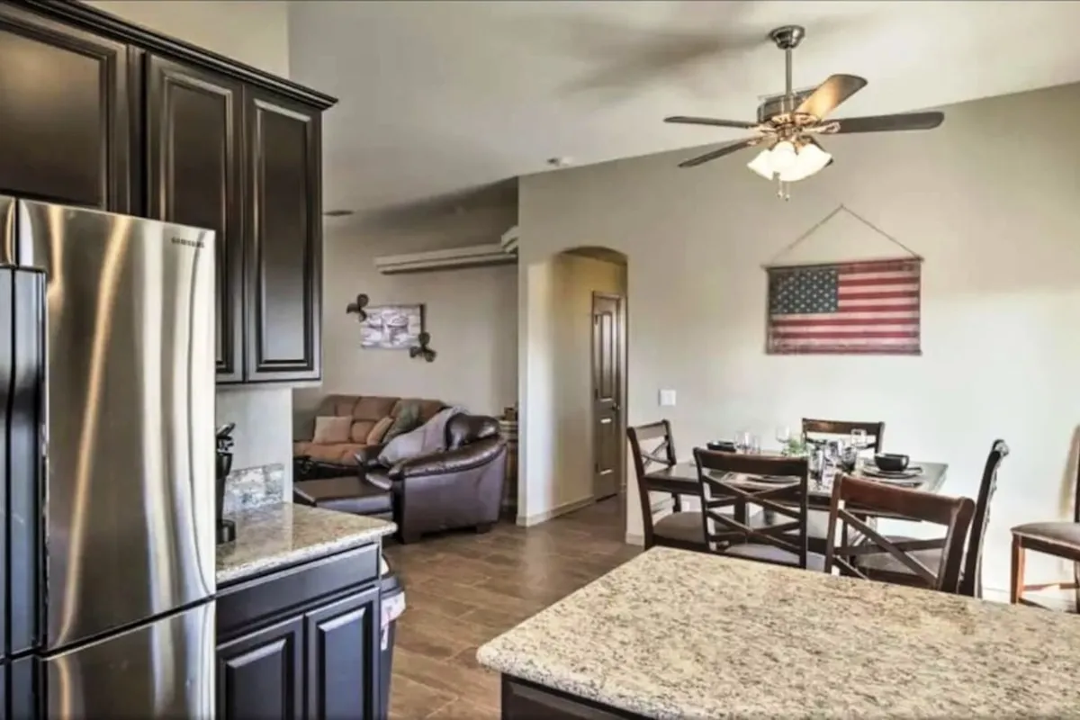 Here, the kitchen flows seamlessly into the dining area. The scene includes a granite countertop, stainless steel refrigerator, and a dining table beautifully set for a meal. American flag-themed decor adds a personal, celebratory touch, suggesting family feasts and social gatherings.