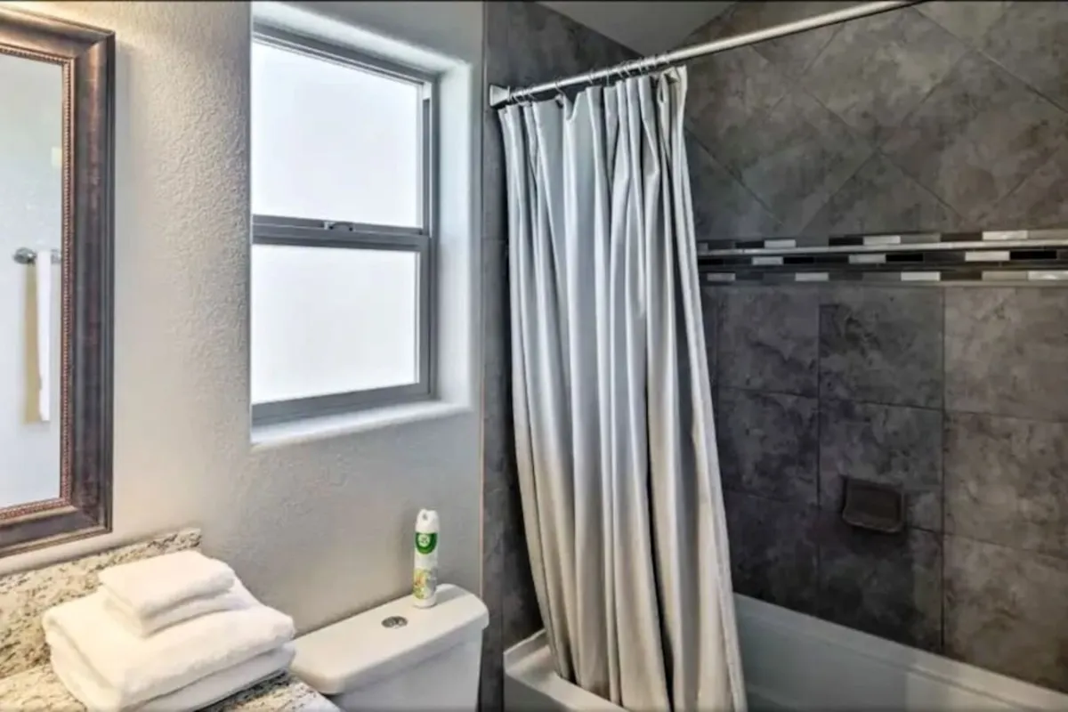 A bright, clean bathroom with a mirror, shower curtain, window, and sink. The room feels fresh and spa-like, suggesting a space ideal for relaxing showers or efficient morning routines.