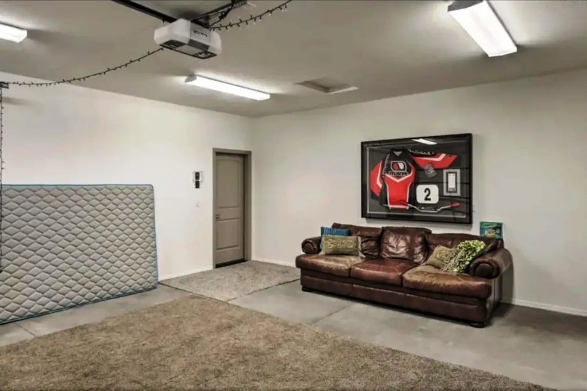 An informal and welcoming interior living space with a leather couch, a framed jersey on the wall, and a visible doorway. The scene suggests relaxation, gathering with friends, or hosting small get-togethers after a night out.