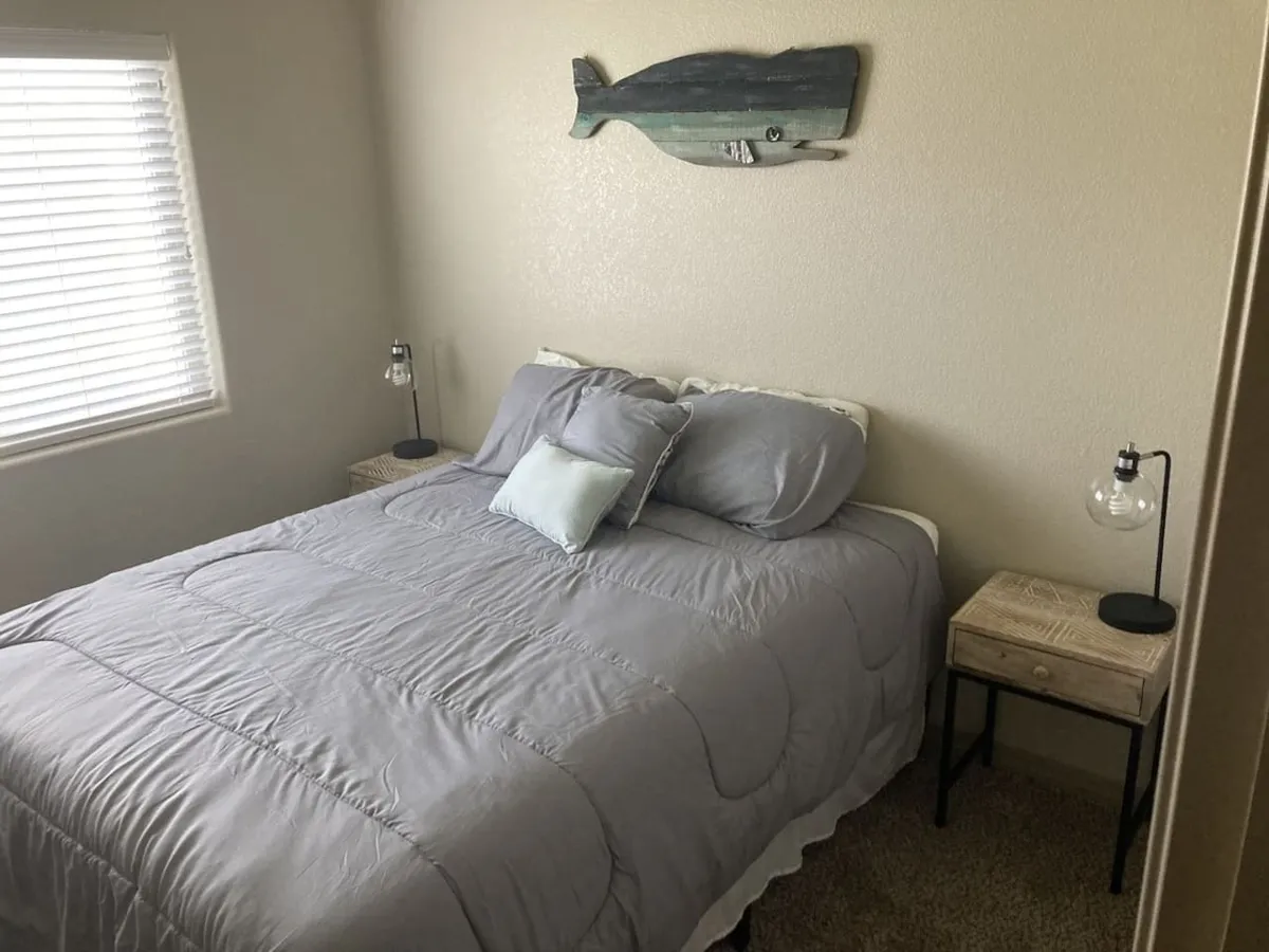 A serene bedroom scene featuring a comfortable bed with neutral bedding, decorative fish art above the headboard, and matching nightstands with warm table lamps. Soft natural light filters into the room, enhancing its tranquil atmosphere and inviting relaxation.