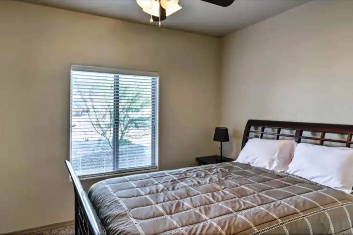 A serene bedroom scene with a cozy bed, a bright window letting in daylight, and a bedside lamp. The space exudes calm and is styled for comfort, encouraging relaxation and undisturbed rest.