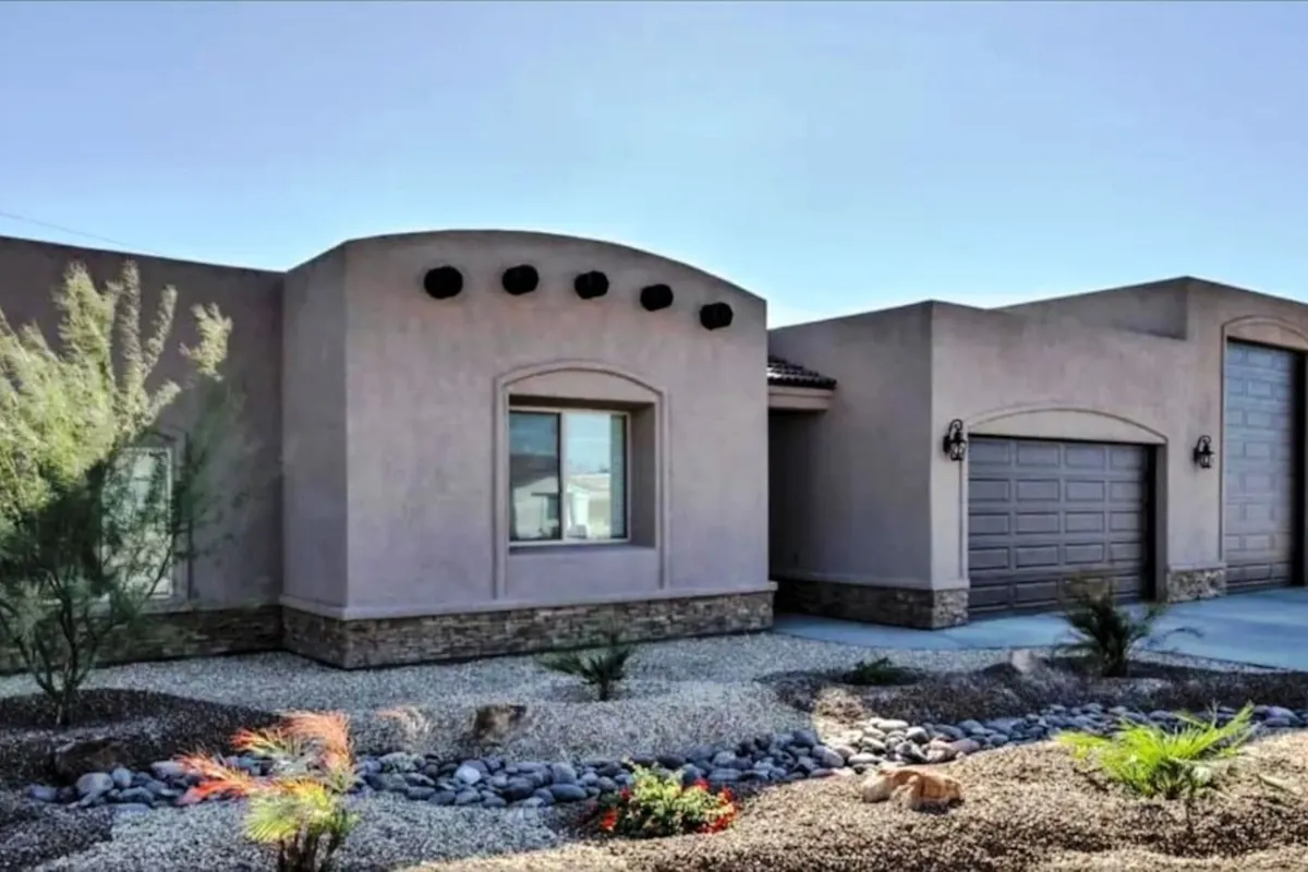 This exterior image showcases a home with a curved roofline, a textured stone foundation, a garage door, and a landscaped front yard. The scene is bright and welcoming, suggesting opportunities for outdoor gatherings and relaxation in the yard.